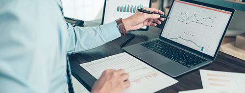 Man examining charts and graphs on his laptop at his desk.